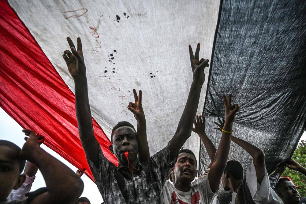 TOPSHOT - Sudanese protesters shout slogans and flash victory signs during a rally outside the army complex in Sudan's capital Khartoum on April 18, 2019. Huge crowds of protesters thronged the Sudanese capital Khartoum today, a week after the army's ouster of president Omar al-Bashir, determined to complete their revolution seeking civilian rule. / AFP / OZAN KOSE