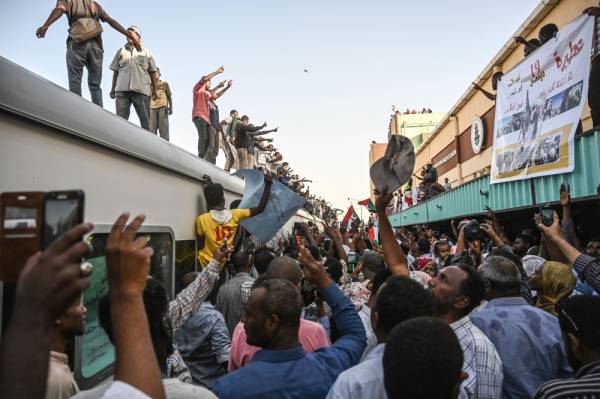 TOPSHOT - Sudanese protesters from the city of Atbara, cheer atop a train, as they arrive at the Bahari station in Khartoum on April 23, 2019. The passengers, who had travelled from the town of Atbara where the first protest against ousted president Omar al-Bashir erupted on December 19, chanted «freedom, peace, justice». Many protesters perched on the roof of the train, waving Sudanese flags as it chugged through north Khartoum's Bahari railway station before winding its way to the protest site, an AFP photographer said. / AFP / OZAN KOSE 