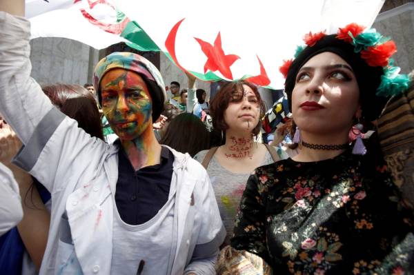 Demonstrators with painted faces hold flags during anti government protests in Algiers, Algeria April 23, 2019. The writing on the neck reads «Algeria is protected by people». REUTERS/Ramzi Boudina