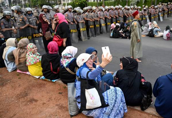 Protesters sit and take photos during a demonstration outside the Elections Oversight Body (Bawaslu) in Jakarta May 21, 2019. Thousands of soldiers fanned out across Jakarta on May 21 after the surprise early announcement of official results in Indonesia's election showed Joko Widodo re-elected leader of the world's third-biggest democracy. / AFP / GOH CHAI HIN 