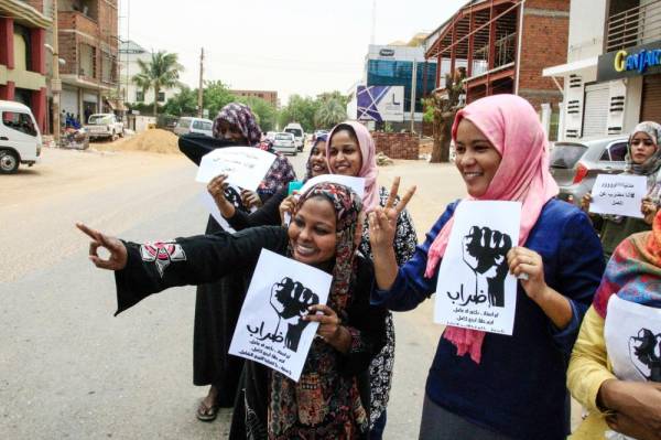 سودانيتان ترفعان علامة النصر ولافتات بالإضراب الذي بدأ في الخرطوم أمس. (أ ف ب)