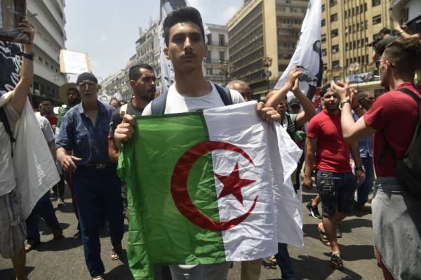 An Algerian demonstrator waves a national flag as he takes part in a protest in the capital Algiers on July 2, 2019. Several hundred Algerian students and teachers demonstrated against the regime today for the 19th consecutive week, and called for the release of «political detainees», including the recently arrested protesters. / AFP / RYAD KRAMDI 