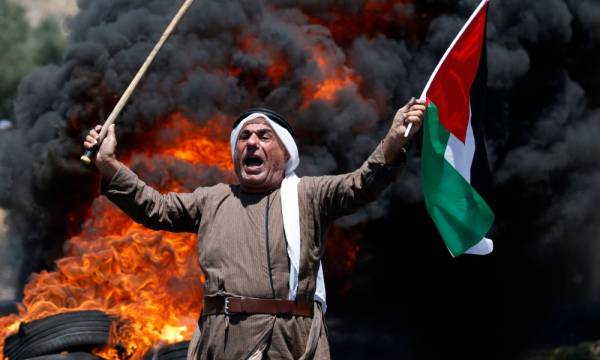 A Palestinian protester holding the national flag and a cane reacts during clashes with Israeli forces following a demonstration against against the expropriation of Palestinian lands by Israel, in the village of Kfar Qaddum, near Nablus in the occupied West Bank, on July 5, 2019. / AFP / JAAFAR ASHTIYEH 