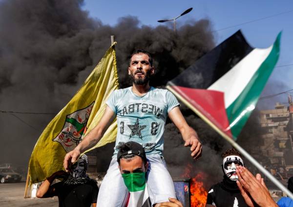 A man is lifted on the shoulders of another using a Palestinian flag as a bandanna, amdist waving flags of Palestine (R) and Palestinian party Fatah (L), as protesters block the main road outside the Palestinian refugee camp of Burj al-Barajneh, south of the Lebanese capital Beirut, on July 16, 2019, during a protest against a decision by the Lebanese government to impose restrictions on the Palestinians' work opportunities. Dozens of Palestinian refugees demonstrated on July 16 against a campaign led by the Labour Ministry to counter the illegal employment of foreigners, despite assurances from the government. / AFP / ANWAR AMRO 