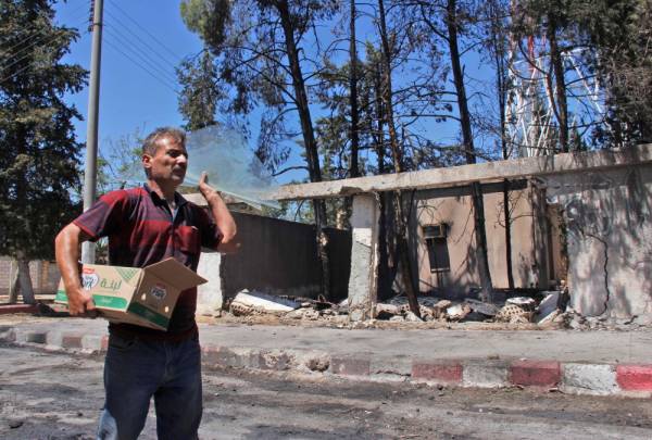 A man carries a broken panes of glass at the site of a explosive-rigged vehicle that detonated in the town of al-Qahtaniyah, in the Hasakeh province on August 7, 2019. A car bombing claimed by the Islamic State group killed five people, including three children, in a Kurdish-held town in northeast Syria on Wednesday, a war monitor said. / AFP / Muhammad AHMAD
