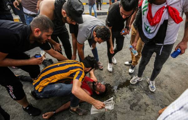 Men gather around a fallen protester affected by tear gas amidst clashes with Iraqi riot police during a demonstration against state corruption and poor services, between the capital Baghdad's Tahrir Square and the high-security Green Zone district, on October 1, 2019. Security forces used water cannons and tear gas to disperse more than 1,000 protesters in central Baghdad. Iraq is considered the 12th most corrupt country in the world according to Transparency International. Power cuts are rampant, water shortages are common and unemployment is high, particularly among youth. / AFP / AHMAD AL-RUBAYE
