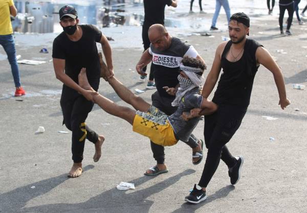 Men carry away a masked protester injured during clashes with riot police during a demonstration against state corruption and poor services, between the Iraqi capital Baghdad's Tahrir Square and the high-security Green Zone district, on October 1, 2019. Security forces used water cannons and tear gas to disperse more than 1,000 protesters in central Baghdad. Iraq is considered the 12th most corrupt country in the world according to Transparency International. Power cuts are rampant, water shortages are common and unemployment is high, particularly among youth. / AFP / AHMAD AL-RUBAYE
