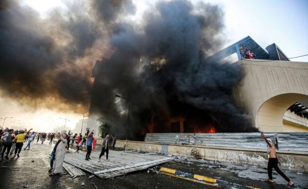 Protesters gather next to a burning building amdist clashes with Iraqi riot police during a demonstration against state corruption and poor services, between the capital Baghdad's Tahrir Square and the high-security Green Zone district, on October 1, 2019. Security forces used water cannons and tear gas to disperse more than 1,000 protesters in central Baghdad. Iraq is considered the 12th most corrupt country in the world according to Transparency International. Power cuts are rampant, water shortages are common and unemployment is high, particularly among youth. / AFP / AHMAD AL-RUBAYE
