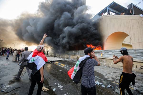 Protesters gather next to a burning building amdist clashes with Iraqi riot police during a demonstration against state corruption and poor services, between the capital Baghdad's Tahrir Square and the high-security Green Zone district, on October 1, 2019. Security forces used water cannons and tear gas to disperse more than 1,000 protesters in central Baghdad. Iraq is considered the 12th most corrupt country in the world according to Transparency International. Power cuts are rampant, water shortages are common and unemployment is high, particularly among youth. / AFP / AHMAD AL-RUBAYE
