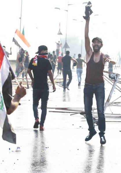 A protester holds a black shirt as he jumps while chanting slogans amidst clashes with Iraqi riot police during a demonstration against state corruption and poor services, between the capital Baghdad's Tahrir Square and the high-security Green Zone district, on October 1, 2019. Security forces used water cannons and tear gas to disperse more than 1,000 protesters in central Baghdad. Iraq is considered the 12th most corrupt country in the world according to Transparency International. Power cuts are rampant, water shortages are common and unemployment is high, particularly among youth. / AFP / AHMAD AL-RUBAYE
