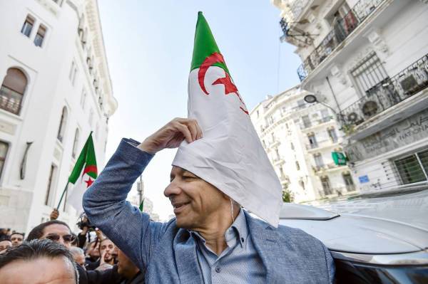 Abdelkader Bengrina, former Algerian tourism minister and presidential candidate for the El-Bina (Construction) Islamist party, is covered by a national flag as he waves to supporters outside his electoral headquarters as he announces the launch of his campaign in the capital Algiers on November 17, 2019. / AFP / RYAD KRAMDI 
