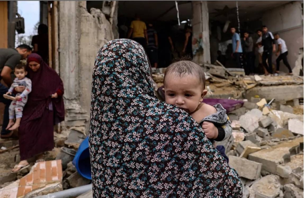 فلسطينية تحمل طفلتها فوق أنقاض الدمار في غزة.