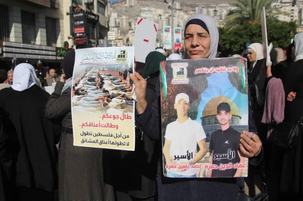 فلسطينية تحمل صورة ابنيها المعتقلين في سجون الاحتلال.